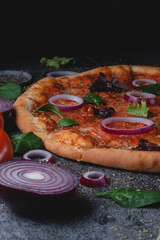 Traditional Italian pepperoni pizza with onions, herbs, tomatoes and cheese on a dark slate table and black background
