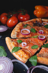 Traditional Italian pepperoni pizza with onions, herbs, tomatoes and cheese on a dark slate table.