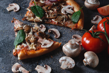 Slices of homemade Italian pizza with mushrooms, ham, tomatoes, cheese, onions and herbs, on a dark slate stone table
