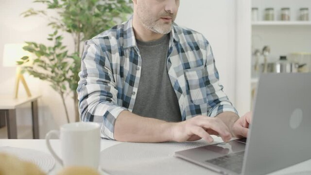 Man typing on laptop, sitting at table, freelancer working on online project