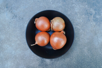 4 raw onions in a black dish is on a grey background

