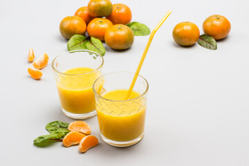 Two glasses with citrus juice, straws in glass. Tangerines on table