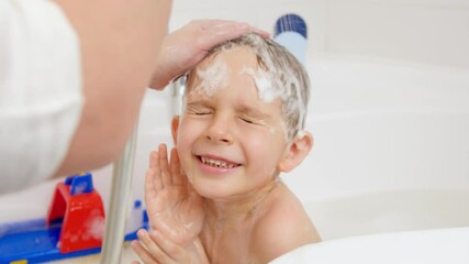Closeup slow motion of mother holding shower head and washing head of her little son sitting in bath. Concept of child hygiene and health care at home. Family having time together and playing at home - Powered by Adobe