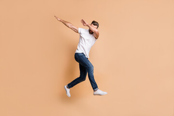 Fototapeta na wymiar Full length body size view of nice tall fit funky guy jumping having fun dab move isolated over beige color background