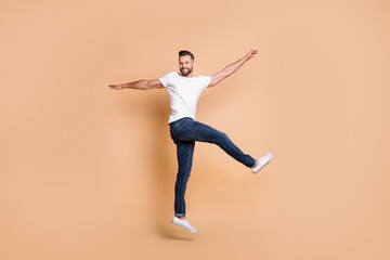 Full length body size view of attractive funky cheerful guy jumping having fun dancing isolated over beige pastel color background