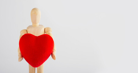 Wooden man holding a heart figurine in his hands on a white background. Wooden mannequin. Valentine's day concept.