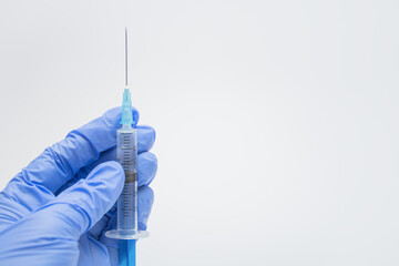 Hand of caring doctor or nurse in blue latex glove holding syringe with drug or vaccine on white or...