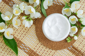White facial mask (face cream, hair mask, body butter, facial cleanser) in the small white jar and white flowers. Natural skin and hair treatment concept. Top view, copy space.