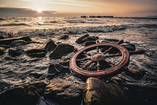Schiffssteuerrad am Strand angesp&uuml;lt nach Schiffsungl&uuml;ck im Sonnenuntergabng