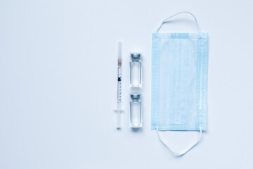 Two glass bottles with liquid , medical mask and syringe on gray background with copy space. The medical conception of combating the covid-19 pandemic. Flu vaccination.  Flat lay