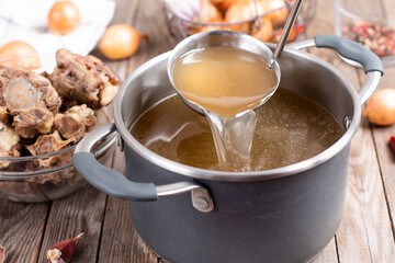 Saucepan with bouillon with a ladle on a wooden table. Bone broth - obrazy, fototapety, plakaty