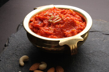 Gajar ka halwa is a carrot-based sweet dessert pudding from India. Garnished with Cashew almond nuts and Served in brass bowl.