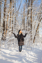 Woman rejoices in the snow in winter pine forest with snow on trees and floor in sunny day