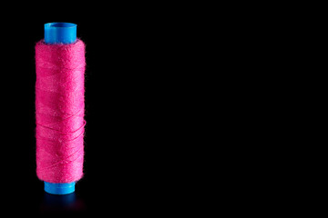Reel with pink sewing silk threads isolated on a black background, close-up, copy space. Bright background for sewing and needlework