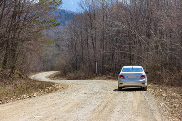 Obraz na płótnie Canvas The car is on a dirt road that goes around a bend in the unknown. A rocky clay road in the Russian forest in spring.