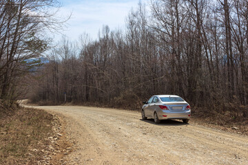Fototapeta na wymiar The car is on a dirt road that goes around a bend in the unknown. A rocky clay road in the Russian forest in spring.