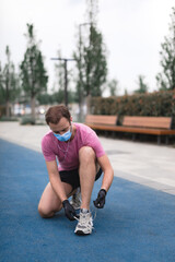 Sportsman with medical mask and gloves, smartphone and earbuds working out, jogging in urban surroundings.