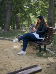Young caucasian female using her smartphone while sitting on a wooden bench in the park