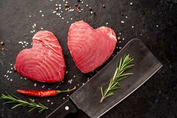 
Two raw tuna steaks with rosemary and spices on a stone background in the shape of a heart with...