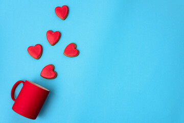 Valentine's Day, red heart shaped cookies on blue paper background flying out from a red  mug tilted  right, flat lay. Love and Valentine's Day concept.