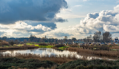 Fototapeta na wymiar The sun shines on the enormous clouds over the lake and the allotment complex in the Buytenpark in Zoetermeer