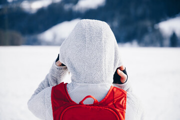 Wandernde, sportliche Person von hinten mit rotem Rucksack, im Hintergrund weiße Schneelandschaft