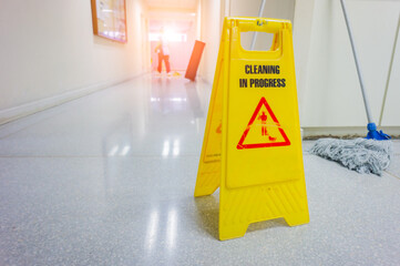 caution wet floor warning sign with blurred worker mopping floor