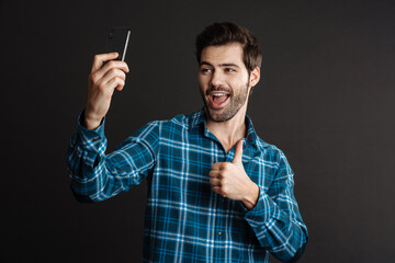 Excited guy showing thumb up while taking selfie on cellphone
