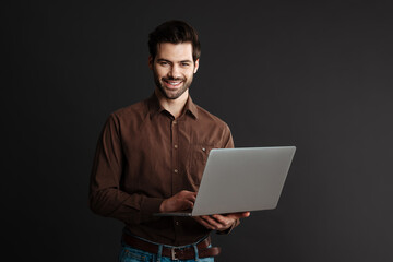 Joyful handsome brunette guy smiling and using laptop