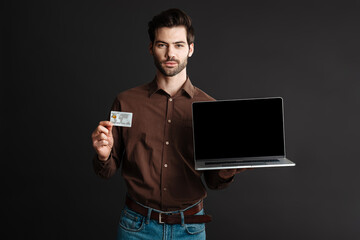 Confident unshaven guy posing with credit card and laptop