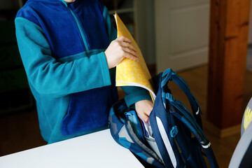 School kid boy getting ready in the morning for school. Healthy child filling satchel with books,...