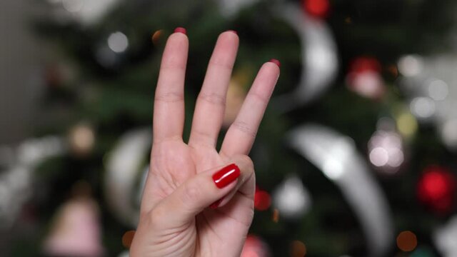 Closeup of hand counting from 0 to 5 isolated on blurry Christmas tree background. Woman shows fist fist, then one, two, three, four, five fingers. Manicured nails painted with beautiful red polish