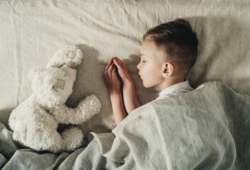 a boy with a white teddy bear sleeps on the bed