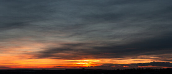 Dramatic gloomy panorama of bright saturated sunset with many dark clouds