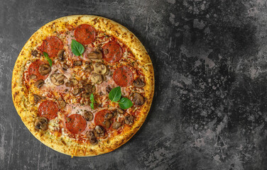 Whole Neapolitan pizza with ham, mushrooms, salami, and cheese served on dark board. Top view, copy space, fast food delivery.