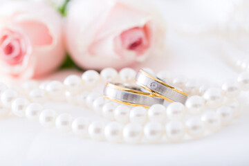 Modern wedding rings with pearl necklace wih pink roses in the background
