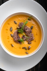 Pumpkin soup with chopped beef and seeds in a white bowl on a dark wooden background