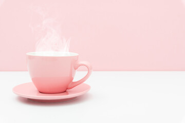 Pink cup with steam, coffee or tea on pink background.