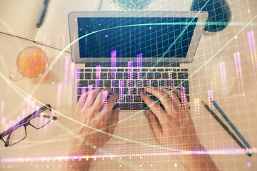 Double exposure of man's hands typing over laptop keyboard and forex chart hologram drawing. Top view. Financial markets concept.