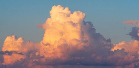 A huge white-pink volumetric cloud in the blue sky.