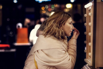 A young woman in front of a mirror adjusts her makeup on her face
