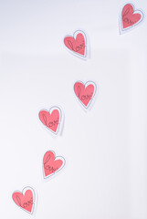 Paper hearts with "love"  written on them, flying like butterflies, on a white background, vertical picture. Concept of love, Valentine