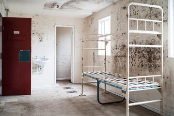 Prison cell block victorian British English jail house with bed in room lock up high security room derelict old new category A B C in custody with bars door open confined escaping incarceration  - obrazy, fototapety, plakaty