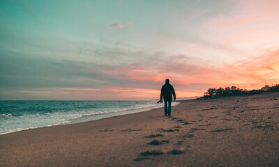 Fototapeta na wymiar Pescatore passeggia sulla sabbia in riva al mare al tramonto.