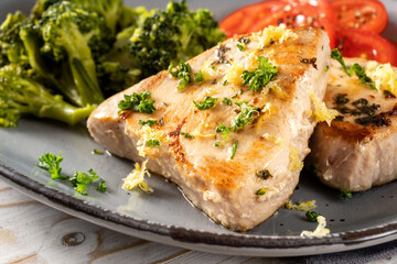 Slice of fried tuna with parsley and lemon zest, broccoli and tomatoes In the background on a gray plate, close-up detail shot with selected focus and narrow depth of field