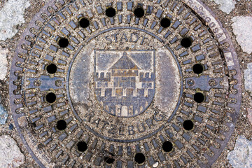 Sandy manhole cover with the coat of arms of the city ratzeburg in a cobblestone street, high angle view from above