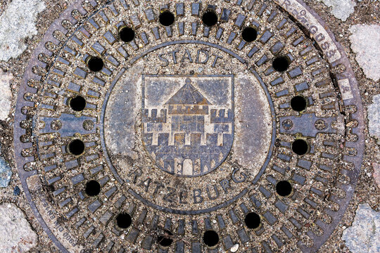 Sandy Manhole Cover With The Coat Of Arms Of The City Ratzeburg In A Cobblestone Street, High Angle View From Above