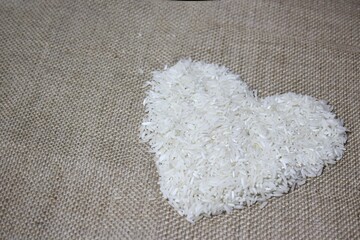 Heart shaped white rice on burlap jute fabric. Selective focus.