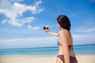 An Asian woman wearing a bikini Takes pictures of herself during her vacation on the beach.selective focus at her