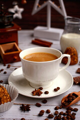 Close- up of a white cup with coffee and coffee beans on a wooden background with a coffee grinder and decor. Vertical